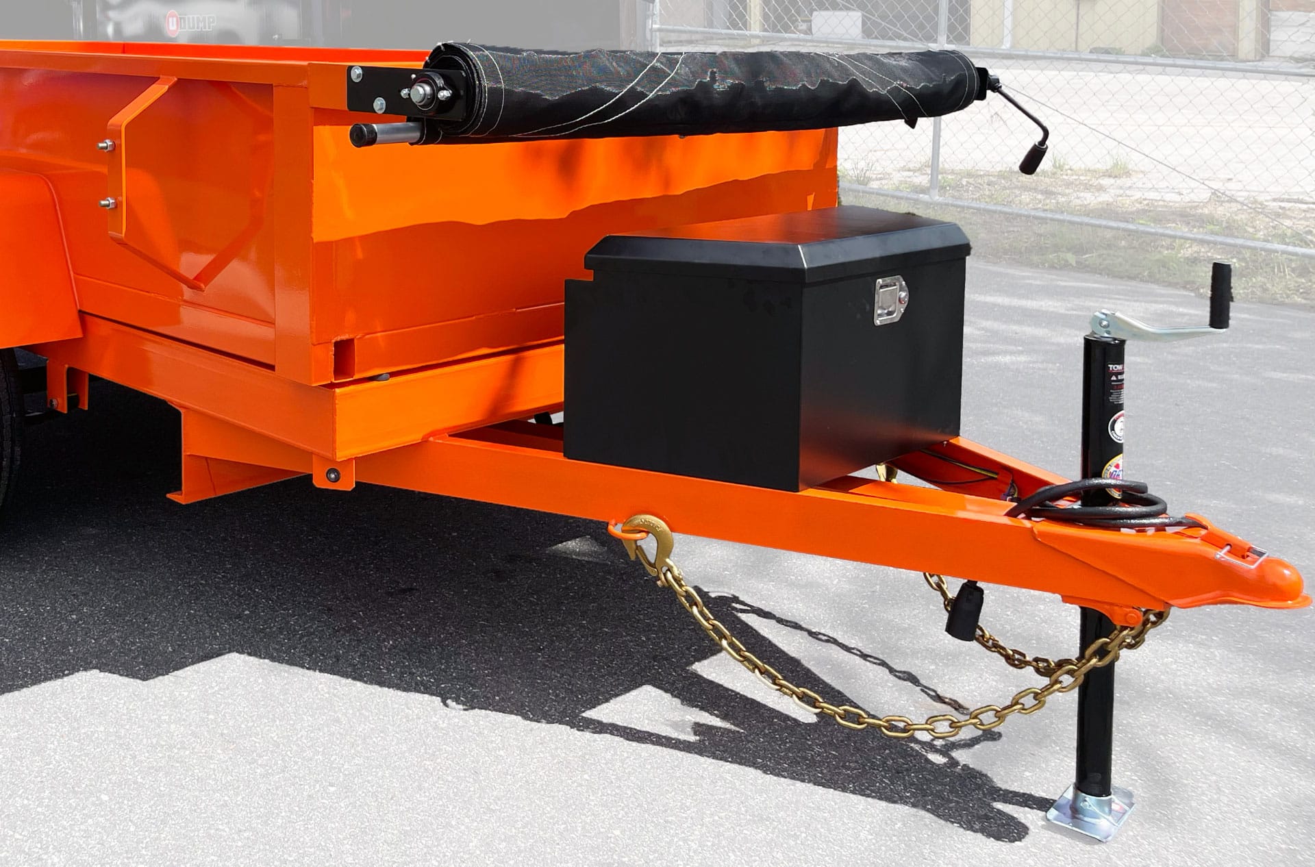 The Rebel Mini Dump Trailer features a bright orange finish, a front-mounted black lock box, rolled-up tarp on top, safety chains, jack stand, and hitch for towing.